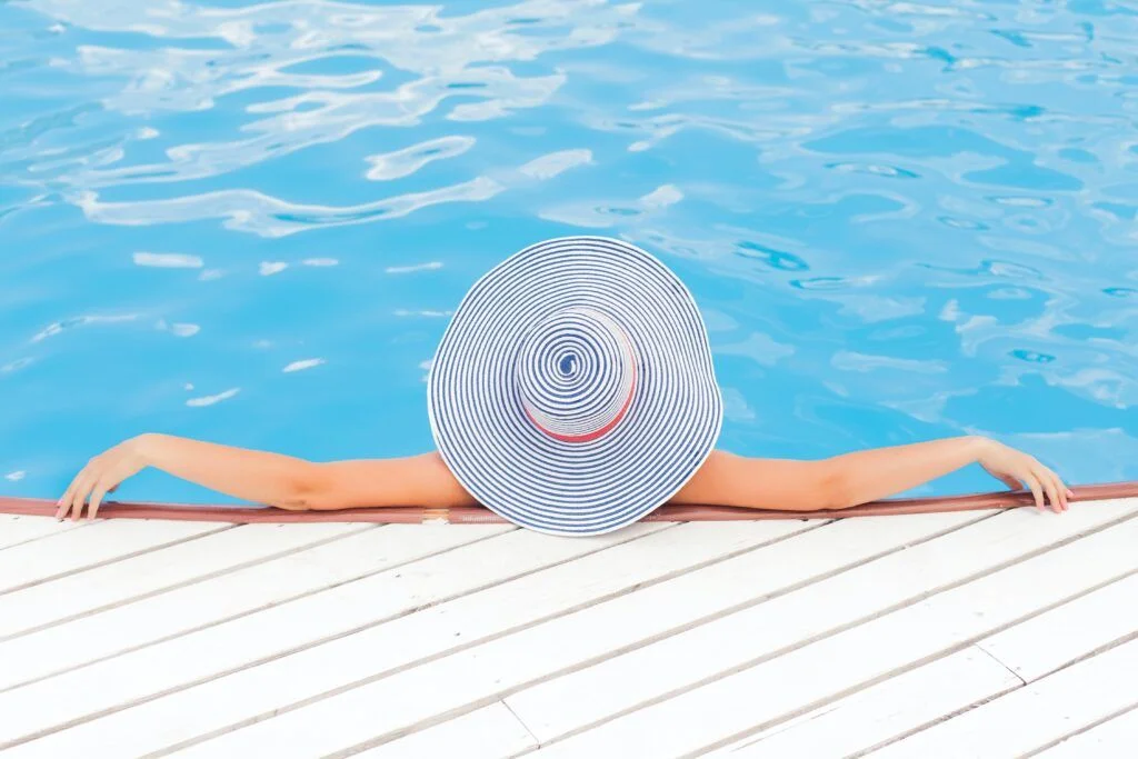 Woman having Multiple sclerosis wearing big hat relaxing in the swimming pool in a warm day