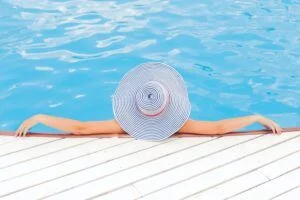 Woman having Multiple sclerosis wearing big hat relaxing in the swimming pool in a warm day